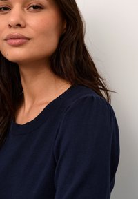 Pull en tricot bleu marine avec un col côtelé et de légères manches bouffantes, présentant une texture lisse et une coupe ajustée.