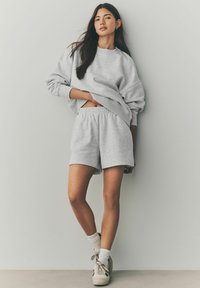 Lichtgrijze oversized sweatshirt en bijpassende shorts van een zachte stof. Kenmerken zijn een ronde halslijn, elastische tailleband en een minimalistisch ontwerp.