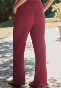 Pantalons bordeaux texturés à forme évasée, dotés de poches latérales et d'une coupe décontractée. Le tissu présente un motif légèrement en relief.
