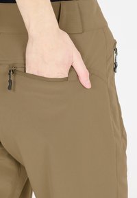 Khaki-byxor tillverkade av lätt material, med en sidficka med en svart dragkedja och slät yta. Handen instoppad i fickan.