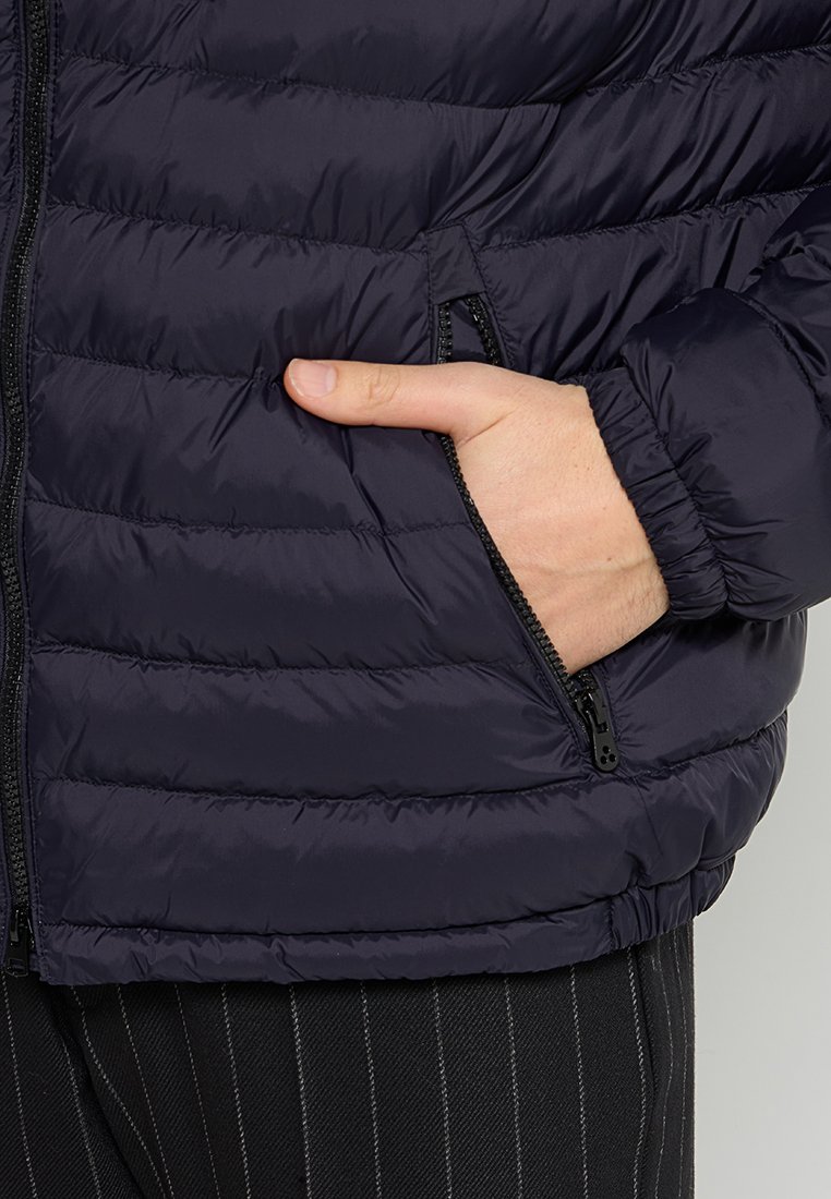 Marineblauwe gewatteerde jas met stikselpatroon, rits aan de voorkant en zakken aan de zijkanten. Voorzien van elastische manchetten en een elastische tailleband voor een aansluitende pasvorm.