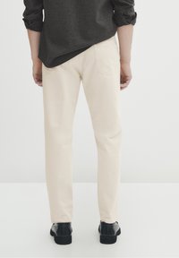 Beiga chinos i bomull, slim fit. Har bakfickor med subtila sömmar. Bärs med en mörk skjorta med uppvikta ärmar och svarta skor.