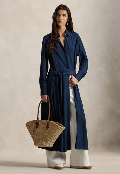 Βραδινό φόρεμα σε χρώμα ναυτικό μπλε με μακριά μανίκια, κουμπιά, ζώνη στη μέση και πλαϊνές σχισμές. Συνδυασμένο με πλεκτή ψάθινη τσάντα χειρός με καφέ δερμάτινες λαβές.