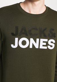 Felpa verde oliva con il grande testo bianco e nero "JACK & JONES." Collo tondo, texture morbida, polsini e orlo a costine.
