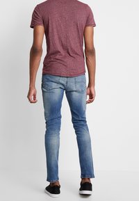 Rotes meliertes T-Shirt, kurze Ärmel, kombiniert mit hellblauem, eng anliegendem Jeans, ausgewaschene Optik, Gesäßtaschen mit Ziernähten, schwarze Sneakers.