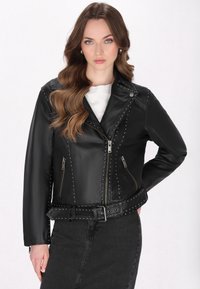 Giacca da motociclista nera in pelle con dettagli in borchie, tasche con cerniera e vita con cintura. Texture liscia, cerniera frontale asimmetrica.