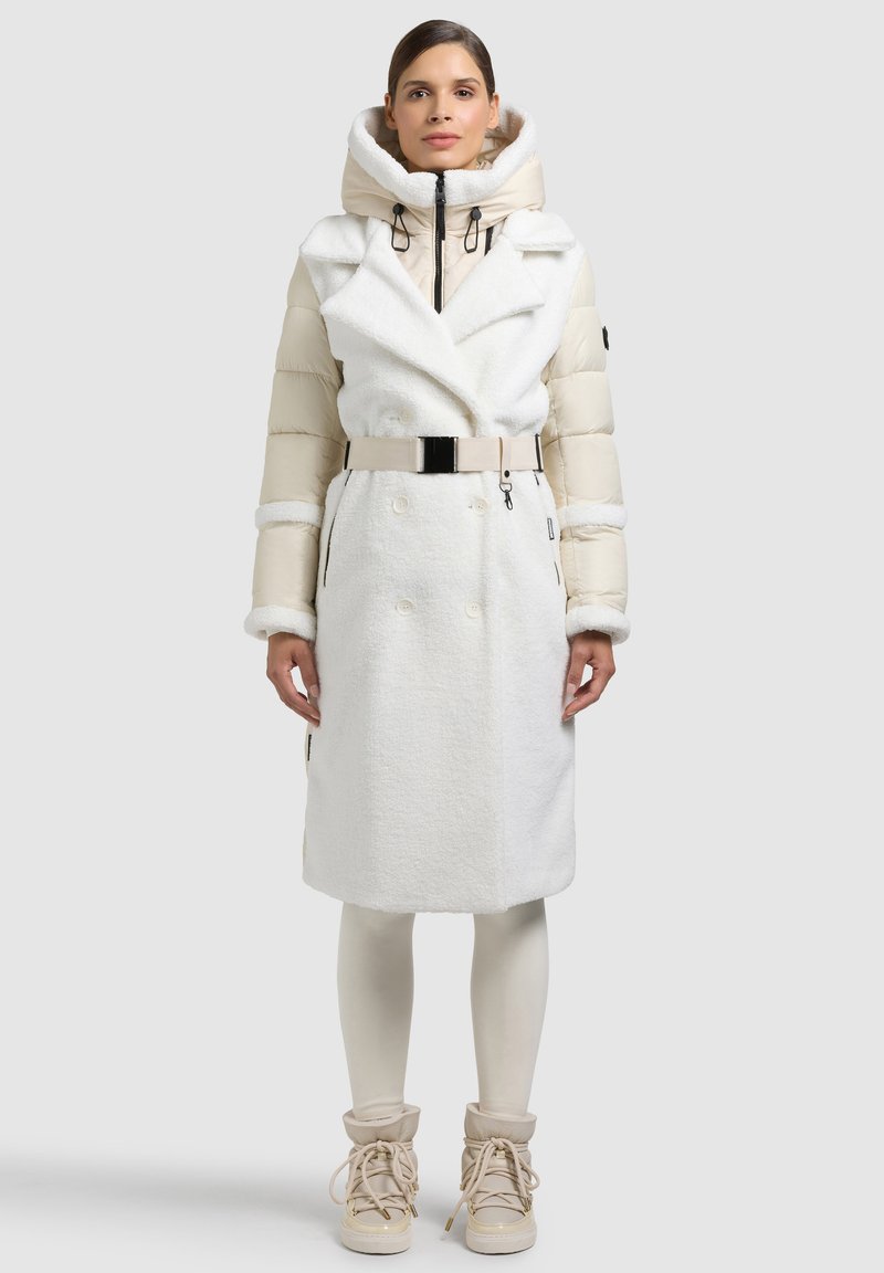 Bílý dvouřadý kabát z měkké, texturované látky, s polstrovanými rukávy a odnímatelnou kapucí. Má pásek a boční kapsy.