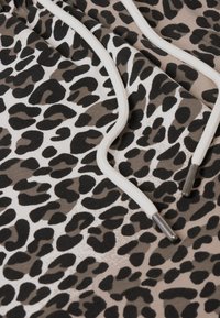 Tela con estampado de leopardo en una mezcla de tonos negro, beige y marrón; cuenta con cordones blancos con puntas de metal. Superficie suave y texturizada.