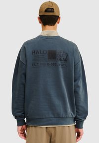 Granatowy sweatshirt o luźnym kroju, z grafiką i tekstem na plecach oraz prążkowanym wykończeniem u dołu. Wykonany z miękkiego materiału, z długimi rękawami i okrągłym dekoltem.