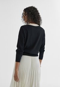Black sweater with long sleeves and a round neckline, paired with a white pleated skirt. The fabric appears soft and lightweight.