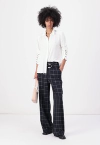 Camisa blanca de botones con aberturas laterales, combinada con pantalones de pierna ancha a cuadros en color navy y un bolso rosa claro. Unos zapatos negros completan el look.