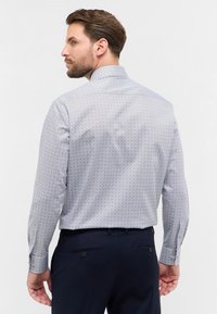 Camicia a maniche lunghe con motivo blu, polsini abbottonati e colletto classico. Realizzata in tessuto leggero, presenta un motivo geometrico.