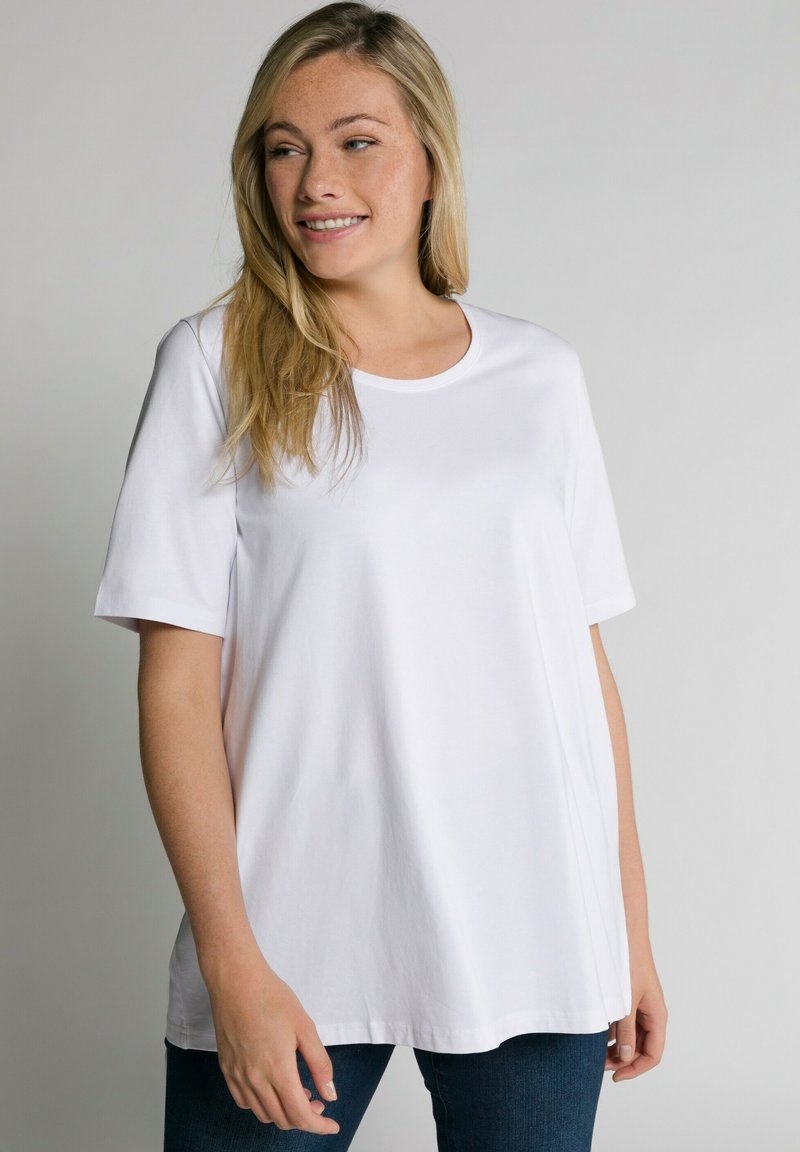 T-shirt bianco a maniche corte, collo rotondo, vestibilità comoda, tessuto in cotone morbido, texture liscia, indossato con jeans scuri, design minimalista.