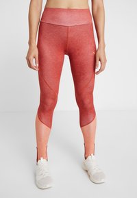 Leggings de sport rouges et dégradés d'orange clair avec une taille haute, un tissu texturé et des fermetures éclair aux chevilles pour faciliter l'enfilage.