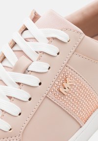 Baskets rose pâle avec lacets blancs, panneau en strass rose doré et logo métallique « MK » sur le côté, vue rapprochée.