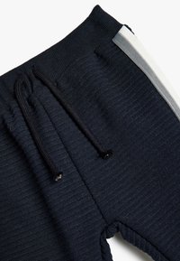 Mørkeblå joggere lavet af ribbet stof, med en snøre i taljen og grå striber på siderne. Blød tekstur med elastiske kanter.