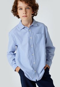 Camisa de botones a rayas azul claro y blanca, con collar, mangas largas y un bolsillo en el pecho, hecha de un tejido fresco.