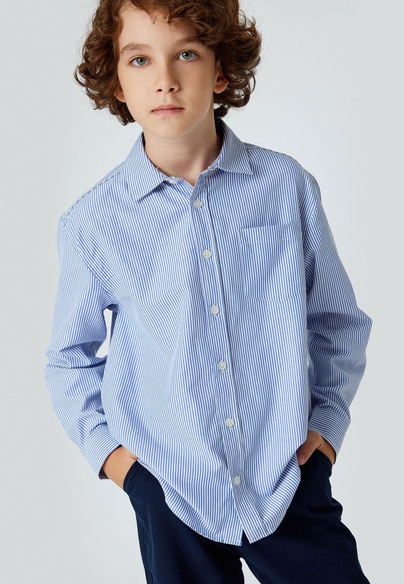 Camisa de botones a rayas azul claro y blanca, con collar, mangas largas y un bolsillo en el pecho, hecha de un tejido fresco.