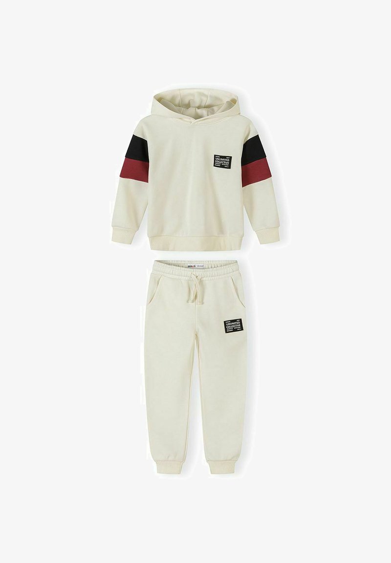 Ensemble sweat à capuche et joggeurs couleur crème avec des rayures noires et rouge foncé sur les manches et des écussons avec le texte "Unlimited Collective" sur la poitrine et la cuisse.