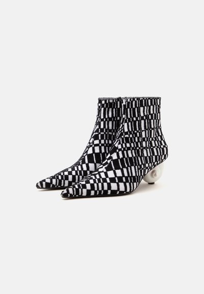 Paire de bottines à carreaux noirs et blancs avec des bouts pointus et des talons ronds en forme de perle sur fond blanc.