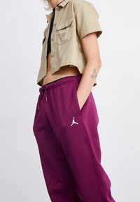 Beige shirt met korte mouwen met twee voorzakken, gedragen met donkerpaarse joggingsbroek met een reliëf witte Jordan-logo op de linker dij.