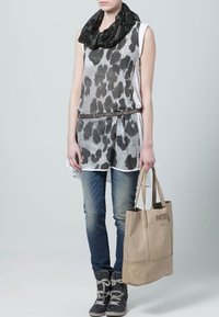 Top grigio leggero senza maniche con stampa animale nera, jeans blu e stivali grigi. Borsa a tracolla beige con logo "DIESEL". Sciarpa nera attorno al collo.
