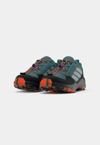 Par de sapatos de corrida em trilhos na cor teal e preta com atacadores laranja e solas com padrão laranja e preto, vistos de um ângulo frontal esquerdo.