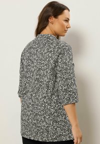 Blusa a righe in bianco e nero con una vestibilità rilassata, maniche a tre quarti e colletto arrotondato. Il tessuto presenta una sottile texture.