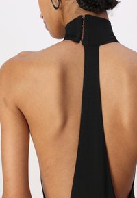Czarna halterowa sukienka z niskim dekoltem na plecach, charakteryzująca się gładką fakturą oraz zapięciem na trzy guziki przy szyi.