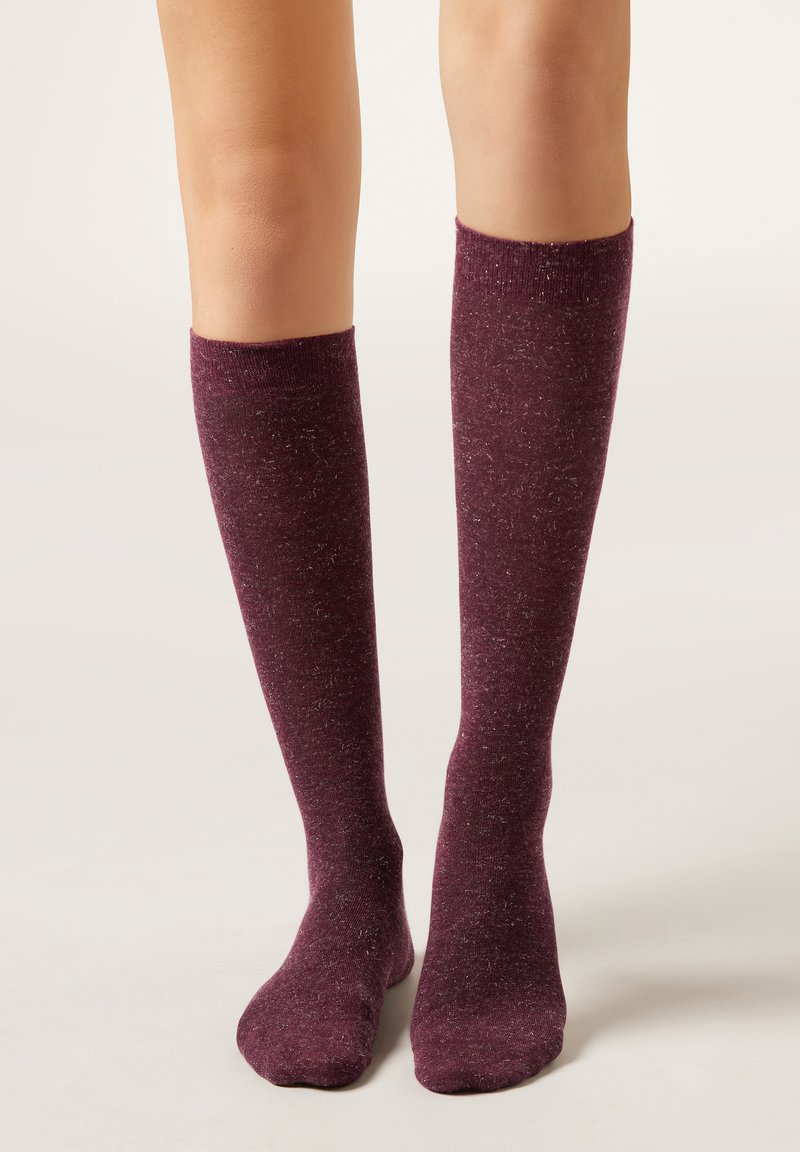 Calze al ginocchio di colore bordeaux intenso con una trama screziata. Realizzate in materiale morbido ed elastico, con una fascia superiore a costine.