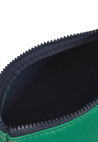 Borsa in tessuto verde con una cerniera nera. L'interno è liscio e scuro, mentre l'esterno presenta un bordo cucito.