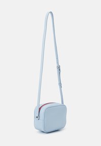 Borsa crossbody azzurro chiaro realizzata in materiale morbido, con forma rettangolare, tracolla regolabile e una zip rossa a contrasto.