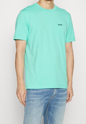 Miętowa bawełniana koszulka z krótkimi rękawami i okrągłym dekoltem, z małym czarnym logo "BOSS" na klatce piersiowej. Noszona z niebieskimi dżinsami.
