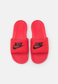 Raudoni Nike šlepetės su plačiu dirželiu, ant kurio yra juodas логотипас, tekstūruotas padas ir suapvalinti kontūrai komfortui.