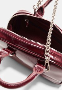 Borsa in pelle verniciata color bordeaux con apertura a zip, hardware in tonalità argento, tracolla a catena e tasca interna. Texture liscia in tutto il prodotto.