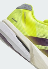 Scarpa da corsa gialla brillante con tomaia in rete testurizzata, dettagli grigi e intersuola bianca. Presenta un design a profilo basso e una striscia viola.