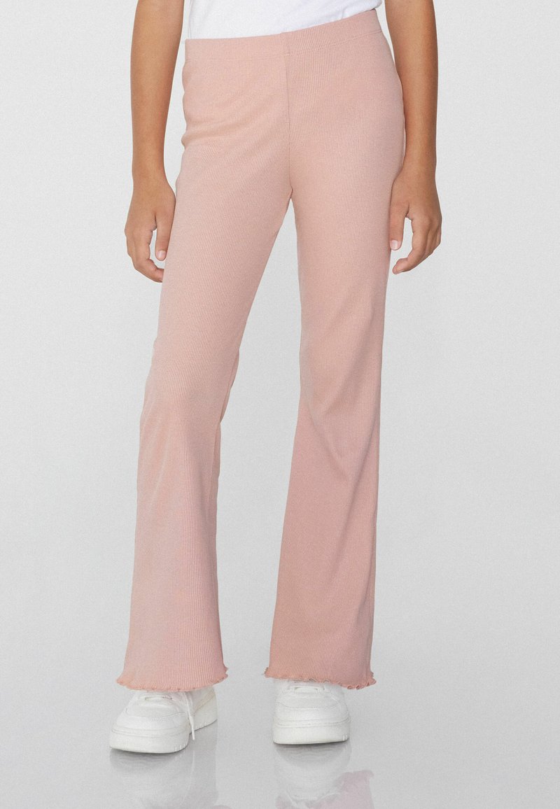 Helle rosa, gerippte, ausgestellte Hose mit fransig geschnittenem Saum aus weichem Stoff, kombiniert mit weißen Sneakern für einen lässigen Look.