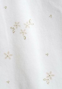 Tessuto bianco con una sottile texture in rilievo, caratterizzato da motivi floreali dorati chiari sparsi e piccoli dettagli dorati.