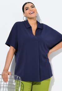 Marineblauwe polo met korte mouwen, met een losse pasvorm en een V-hals, gecombineerd met felgroene broek. Soepele textuur en minimalistisch ontwerp.
