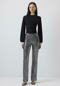 Zwarte lange mouw top met een gedraaide ontwerp, gecombineerd met glanzende, zilveren pailletten broek. Heeft een aangesloten silhouet en hakken met enkelriem.