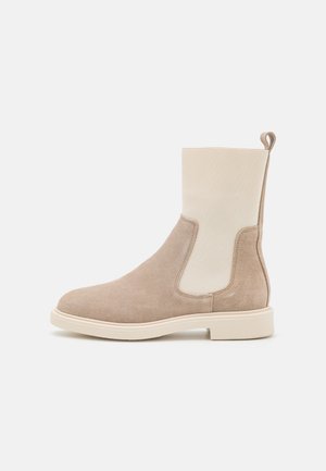 Beige ruskind Chelsea-støvle med cremefarvet elastisk sidepanel, trækflig bagpå og en flad gummisål.