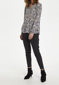 Blouse longue à manches longues avec un décolleté en V, présentant des motifs bleus, jaunes et noirs. Associée à un pantalon cargo noir ajusté et des bottines.