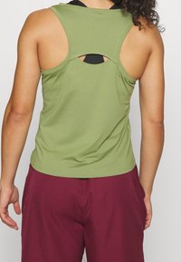 Oliwkowy bezrękawnik o ryflowanej fakturze, z wycięciem w kształcie łezki na plecach. W połączeniu z bordowymi spodniami.