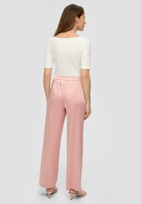 Witte, getailleerde top met korte mouwen, gecombineerd met lichtroze wijde broek. Gladde textuur, minimalistisch ontwerp en taps toelopende zoom.