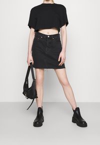 Czarny skrócony t-shirt, dopasowana dżinsowa mini spódnica z postrzępionym hemem, w połączeniu z masywnymi czarnymi botkami za kostkę oraz małą czarną torebką na ramię.