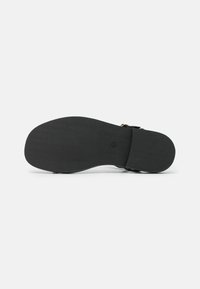 Suola di scarpa nera con superficie testurizzata, caratterizzata da una forma arrotondata e un tacco leggero. Include un'impronta di logo circolare.