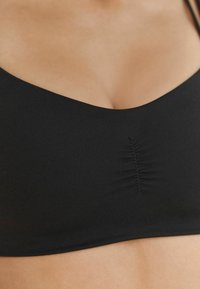 Bralette in tessuto elasticizzato nero con scollatura a V e dettaglio centrale arricciato. Texture liscia con spalline regolabili.