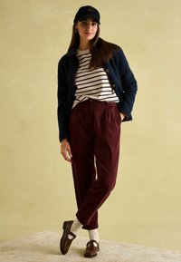 Marineblau strukturierte Jacke, gestreiftes cremefarbenes und marineblaues Hemd, burgunderfarbene Cordhosen, braune Schuhe und Socken mit Punkten. Einfache Accessoires inklusive.