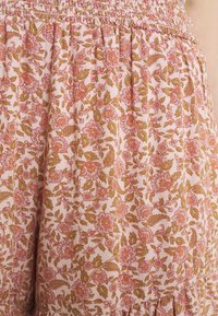 Tissu léger à motif floral avec des teintes de rose et de vert ; taille froncée et ourlet volanté ; présente des petites fleurs et des accents feuillus.