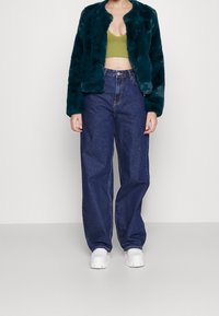 Veste en fausse fourrure teal, design court ; haut en tricot olive ; jeans bleu taille haute, ample ; baskets blanches à semelles épaisses.